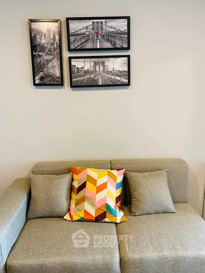 Modern living room with stylish gray sofa and colorful geometric pillow, framed cityscape art on wall.