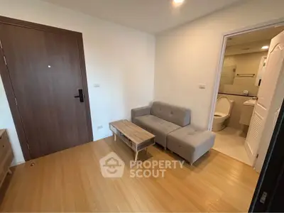 Cozy apartment entrance with modern sofa and wooden flooring, adjacent to a compact bathroom.