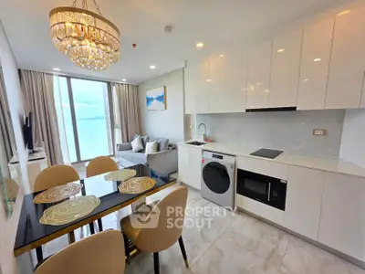 Modern open-plan kitchen and living room with elegant chandelier and sea view.