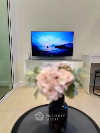 Modern living room with TV and elegant decor, featuring a sleek white cabinet and stylish floral arrangement.