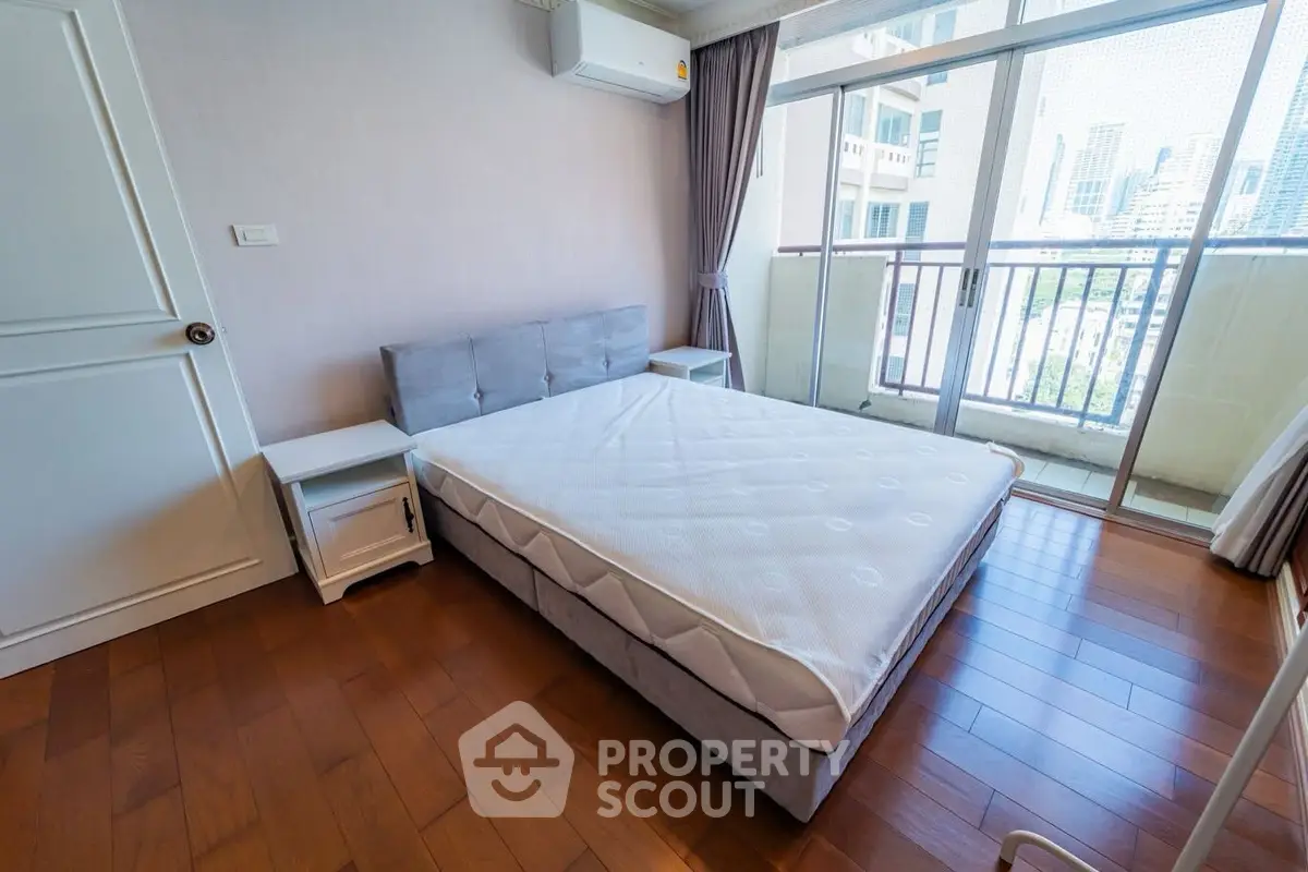 Spacious bedroom with balcony and city view, featuring hardwood floors and modern furnishings.