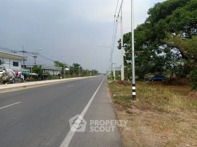 Expansive road view with adjacent greenery and distant buildings, ideal for real estate development.