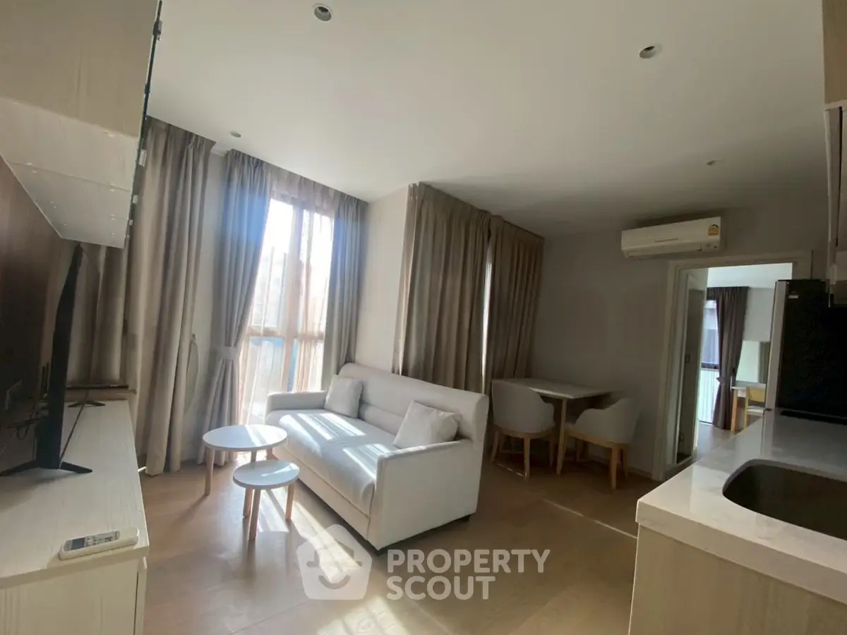 Modern living room with natural light, cozy sofa, and dining area in open layout apartment.