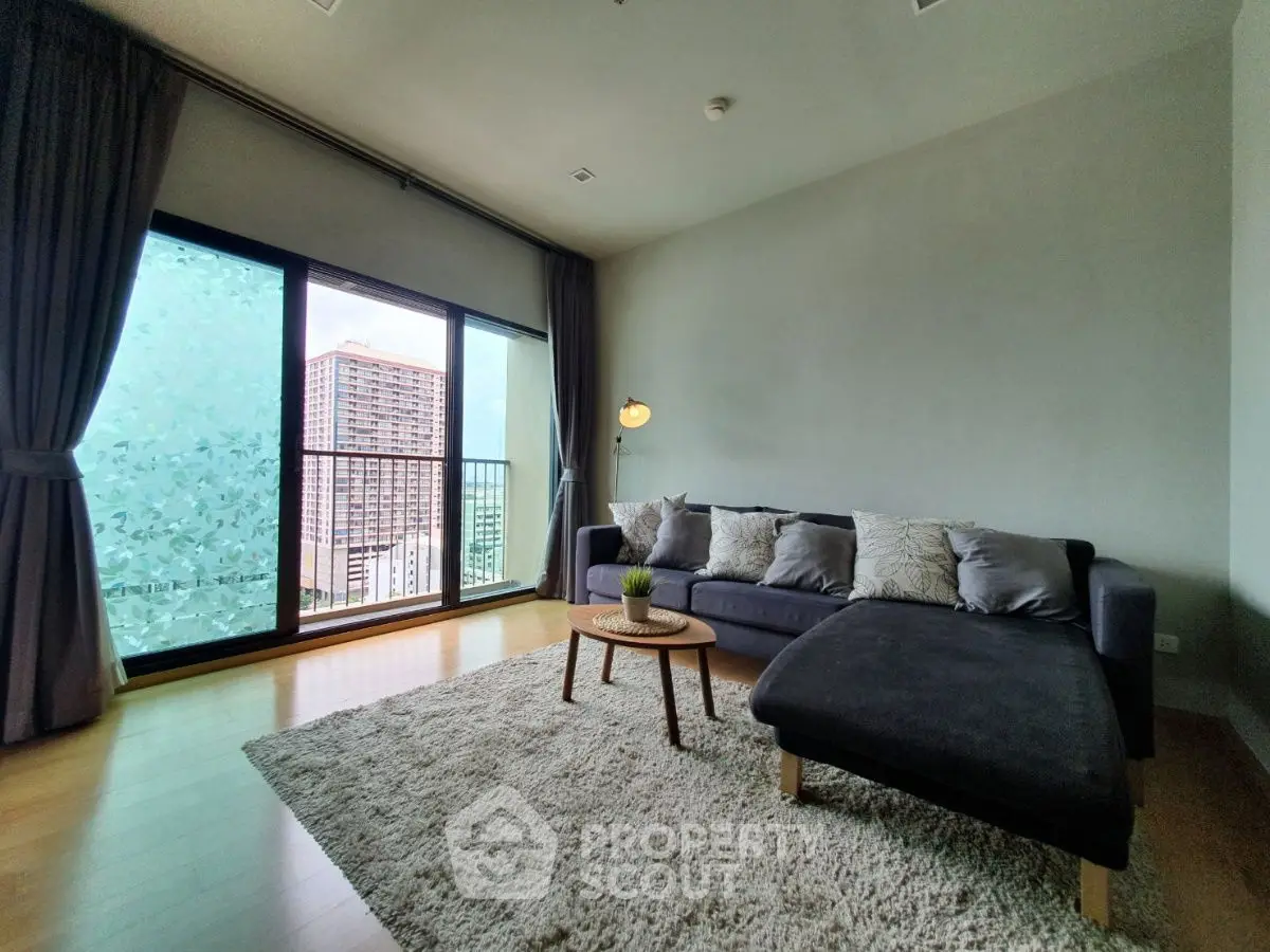 Spacious living room with large window and modern furniture in a high-rise apartment.