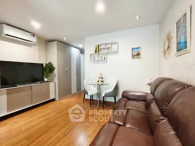 Modern living room with leather sofa, flat-screen TV, and dining area in a cozy apartment.