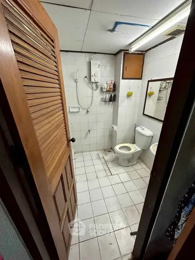 Compact bathroom with shower, toilet, and water heater in a cozy real estate unit.