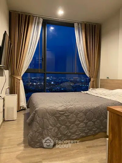 Cozy bedroom with stunning city view through large windows at night.