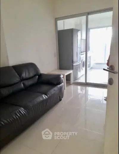 Modern apartment with sleek leather sofa and glass sliding doors leading to a bright kitchen area.