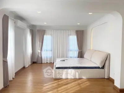 Spacious bedroom with elegant curtains and natural light, featuring a comfortable bed and wooden flooring.