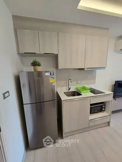 Modern compact kitchen with sleek cabinetry and stainless steel fridge in a stylish apartment.