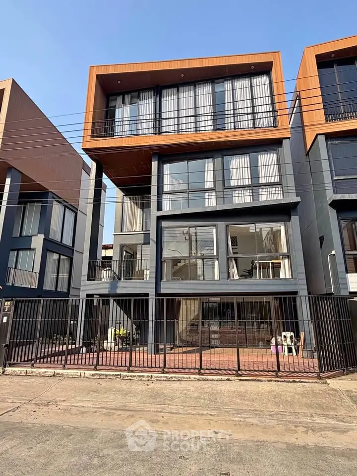 Modern multi-story building with large windows and sleek design, featuring a gated entrance and contemporary architecture.