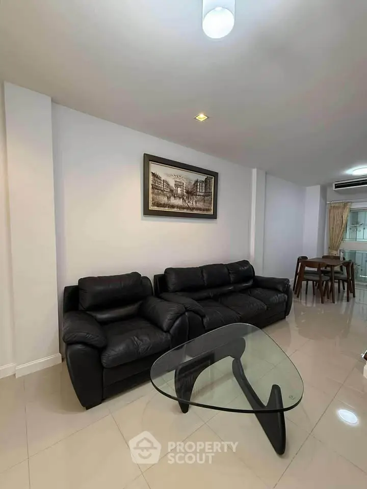 Modern living room with sleek black leather sofa and stylish glass coffee table, perfect for urban living.