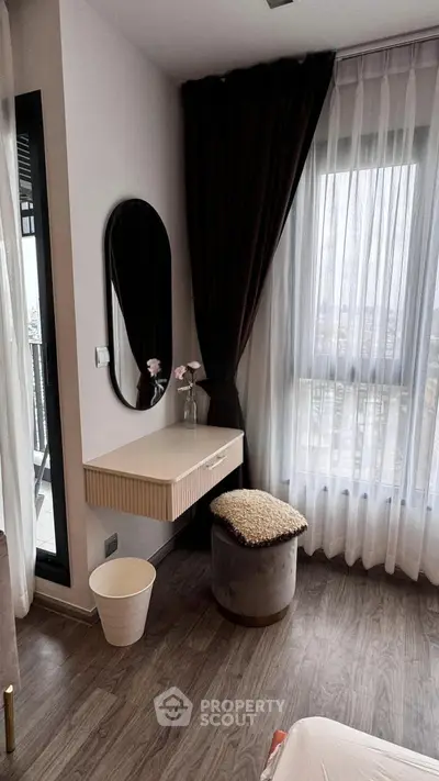 Chic bedroom corner with vanity, plush stool, and floor-to-ceiling windows offering natural light and city views.