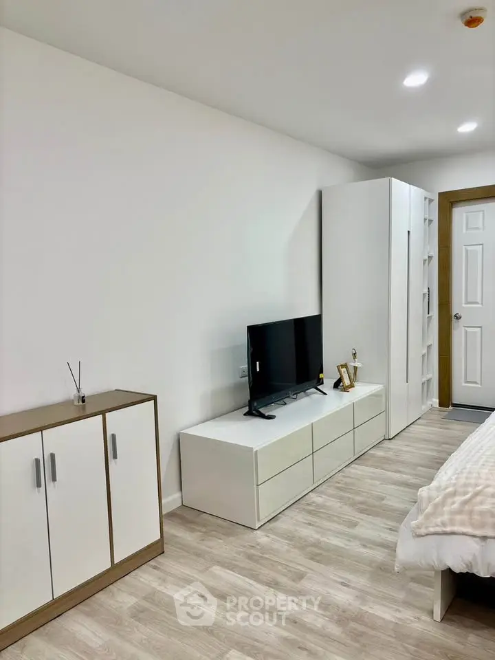 Modern bedroom with sleek furniture and minimalist decor, featuring a flat-screen TV and ample storage space.