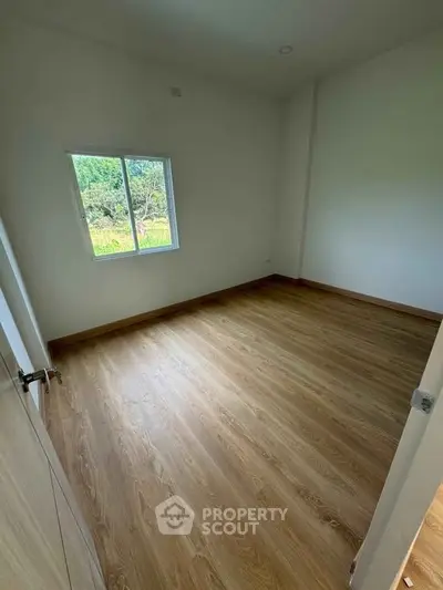 Spacious empty bedroom with wooden flooring and a scenic window view.