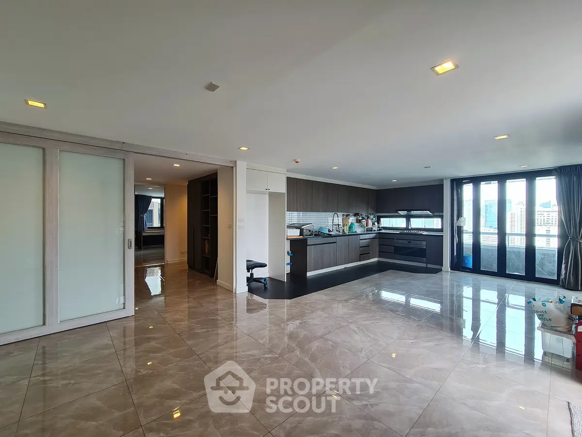 Spacious open-plan living room with modern kitchen and city view, featuring sleek tile flooring and ample natural light.