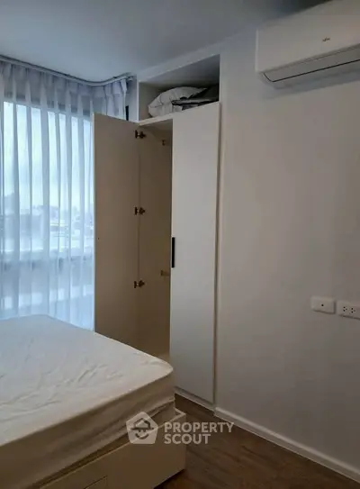 Modern bedroom with built-in wardrobe and air conditioning, featuring a large window with sheer curtains.