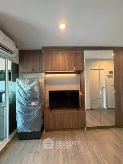 Modern living room with sleek wooden cabinetry and mirrored closet doors, featuring a compact kitchen area.