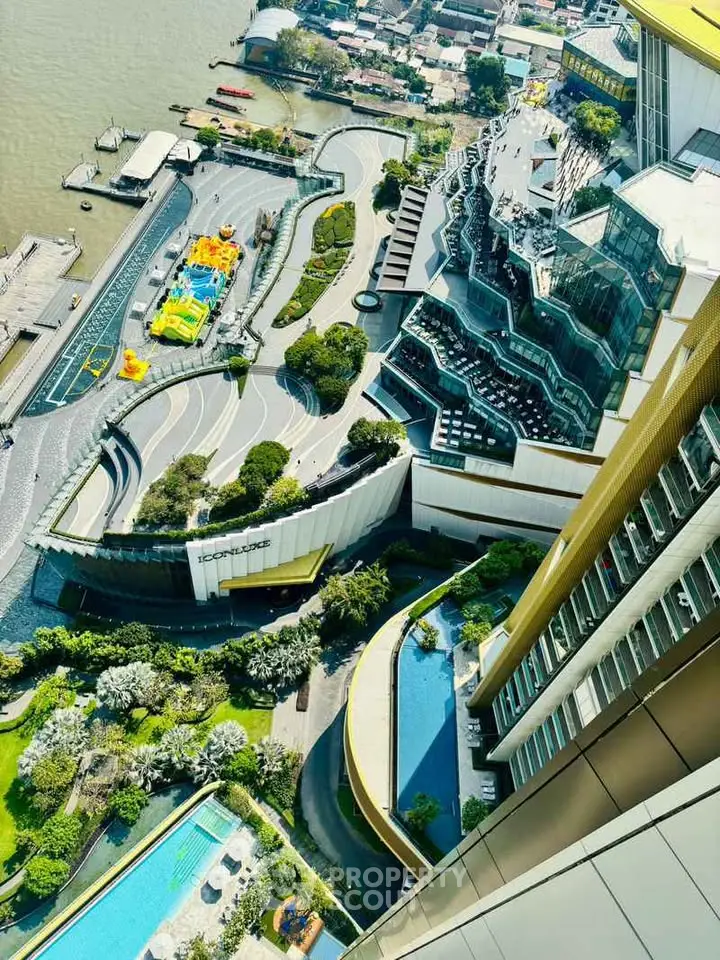 Stunning aerial view of modern riverside building with lush gardens and pool, showcasing unique architectural design.