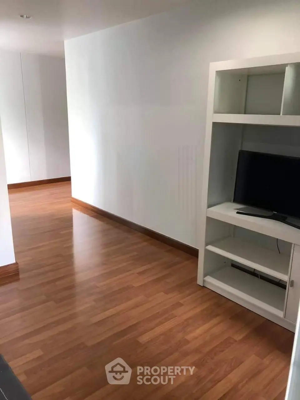 Spacious modern living area with wooden flooring and built-in shelving unit.