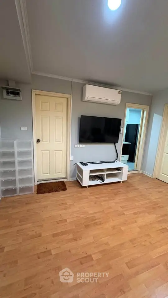 Spacious living room with wooden flooring and modern TV setup in a cozy apartment.