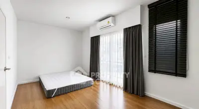 Minimalist bedroom with floor mattress, wooden flooring, and large window with curtains.
