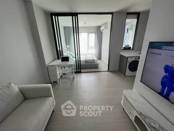Modern living room with sleek design and open layout, featuring a cozy bedroom view through glass doors.