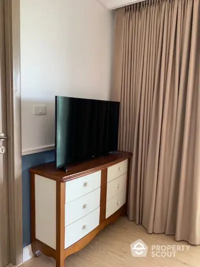 Cozy living space with modern flat-screen TV on a stylish two-tone cabinet, complemented by elegant floor-length curtains.