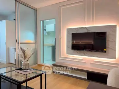 Modern living room with stylish decor and open kitchen layout, featuring a sleek TV setup and elegant lighting.
