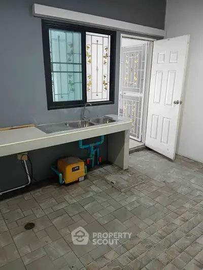 Spacious kitchen with modern sink and tiled flooring, featuring a secure window and door.