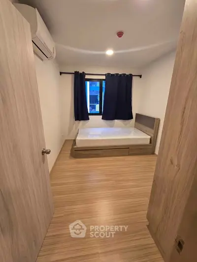 Cozy bedroom with wooden flooring and modern air conditioning unit, perfect for a comfortable living experience.