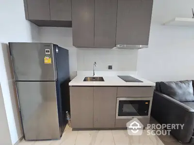 Modern kitchen with sleek stainless steel refrigerator and built-in oven, complemented by stylish gray cabinetry and a cozy living area with a plush sofa.