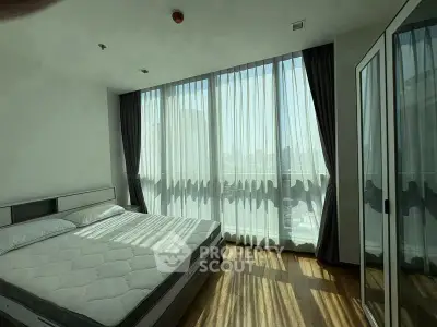 Spacious bedroom with floor-to-ceiling windows and city view, featuring elegant curtains and wooden flooring.