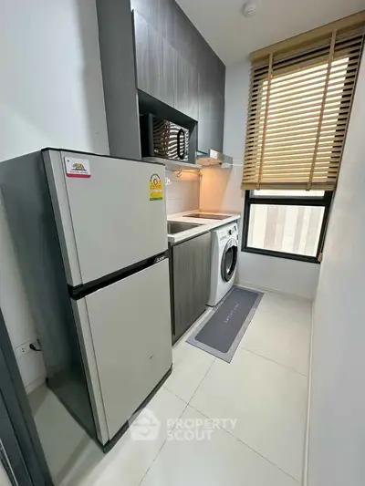Modern compact kitchen with fridge, washing machine, and microwave in sleek design.