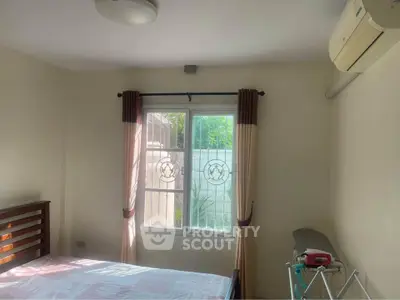Cozy bedroom with window view, air conditioning, and ironing board, perfect for comfortable living.