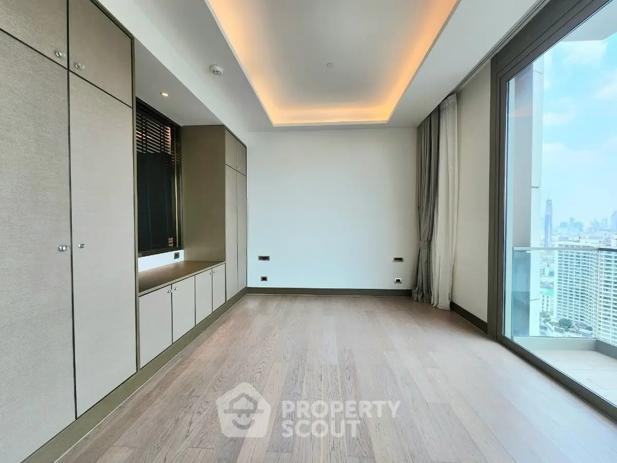 Spacious modern room with large windows and city view, featuring elegant wood flooring and built-in storage.
