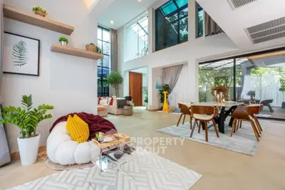 Luxurious open-plan living and dining area with high ceilings and modern decor, featuring large windows and elegant furnishings.