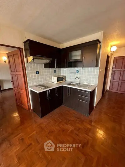 Charming kitchen with dark wood cabinets and parquet flooring, featuring a compact open layout.
