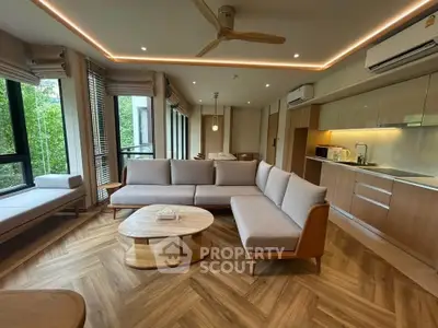 Modern living room with stylish furniture and open kitchen layout, featuring large windows and wooden flooring.