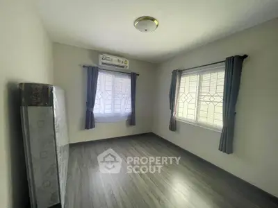 Spacious unfurnished bedroom with polished wooden flooring, large windows with stylish curtains, and a serene neutral color palette awaiting personalization.