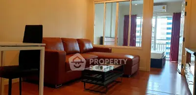Spacious living room with modern leather sofa and glass coffee table, leading to a bright bedroom.