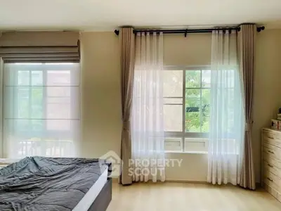 Spacious bedroom with large windows and elegant curtains, offering abundant natural light and serene views.