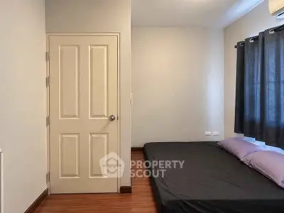 Minimalist bedroom with wooden flooring and simple decor, featuring a low-profile bed and neutral tones.