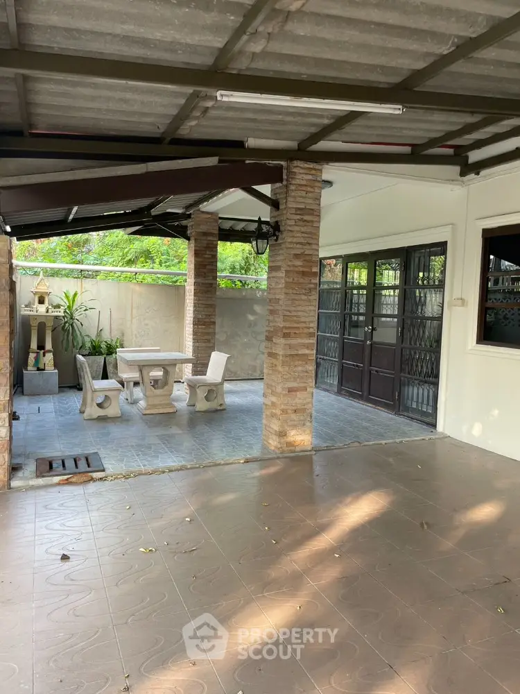 Charming covered patio with stone pillars and outdoor seating in a serene garden setting.