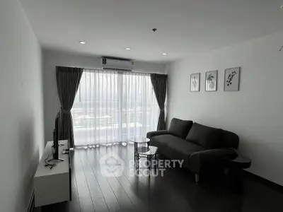 Modern living room with sleek black sofa, stylish decor, and large window offering natural light.