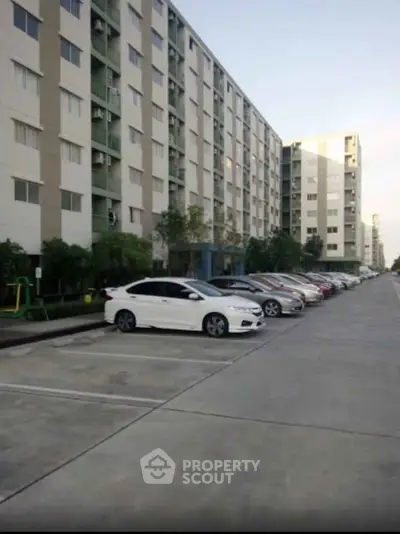 Modern apartment building with spacious parking area and multiple parked cars.