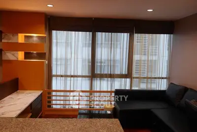 Modern living room with large windows and stylish black sofa in a cozy apartment.