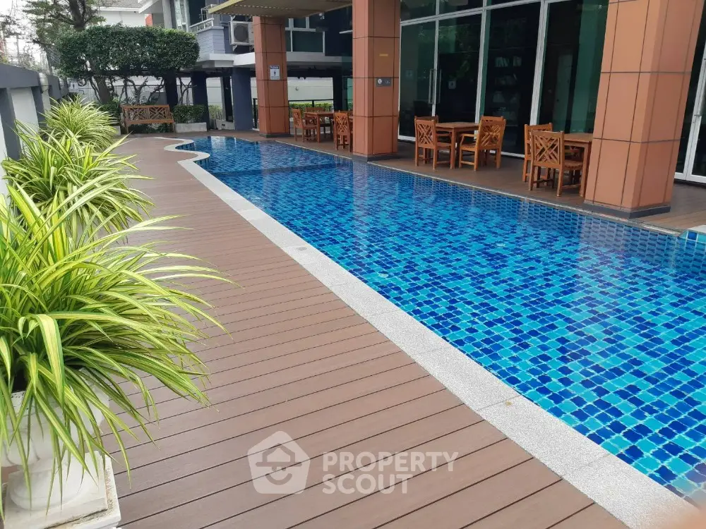 Luxurious poolside area with modern wooden deck and vibrant blue tiles in a high-end residential complex.
