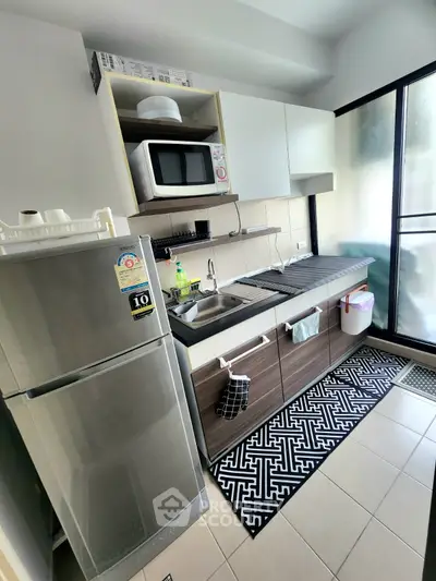 Modern kitchen with sleek cabinetry, stainless steel fridge, and microwave in a compact layout.