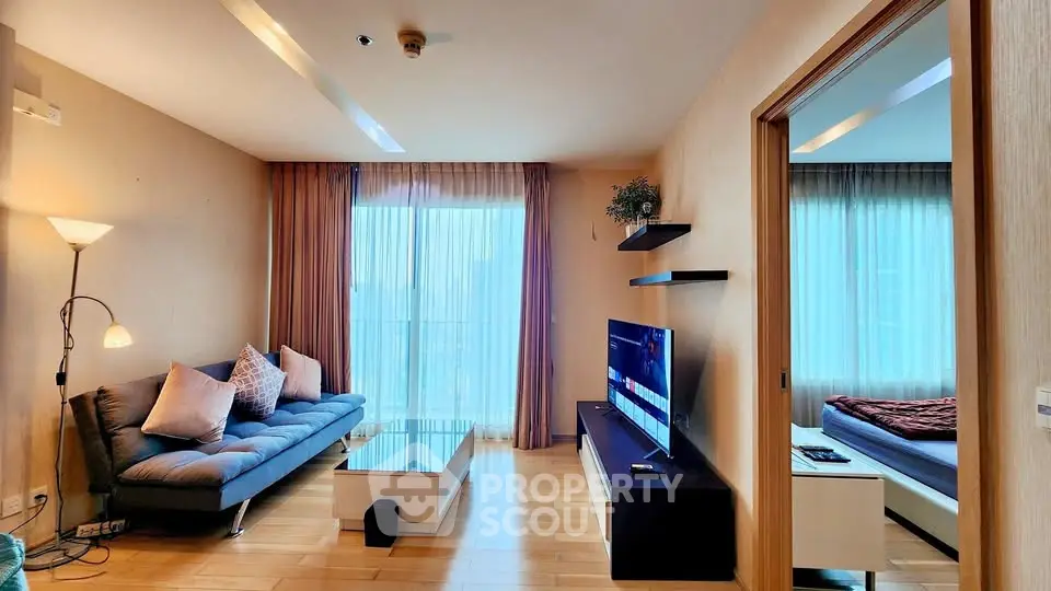 Modern living room with cozy sofa and TV, adjacent to a bedroom with natural light.